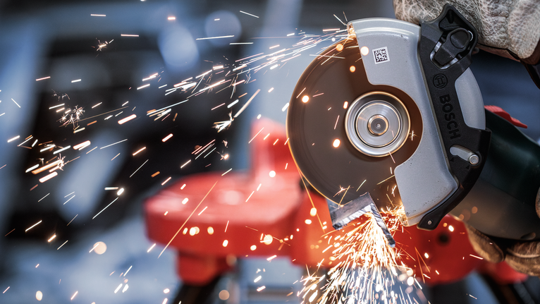 PRO Metal Bonded Cutting Disc, 125 x 1.6 x 22.23 mm, X-Lock A person wearing safety equipment uses an angle grinder to cut metal, producing sparks.