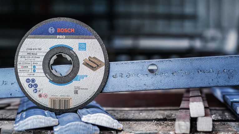 PRO Metal Bonded Cutting Disc, 125 x 1.6 x 22.23 mm, X-Lock Cutting disc placed upright next to a metal bar with a hole in a workshop.