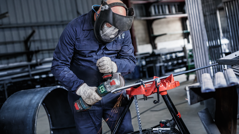 PRO Metal Bonded Cutting Disc, 125 x 1.6 x 22.23 mm, X-Lock A person wearing safety equipment uses an angle grinder to cut metal, producing sparks.