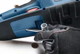 A person wearing safety equipment uses a wrench to adjust a cordless chainsaw.