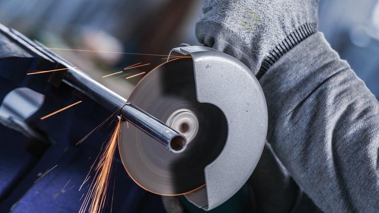 PRO Multi Material X-Lock Cutting Disc, 125 x 1 x 22.23 mm Person wearing safety equipment cutting a metal pipe with a grinding tool.