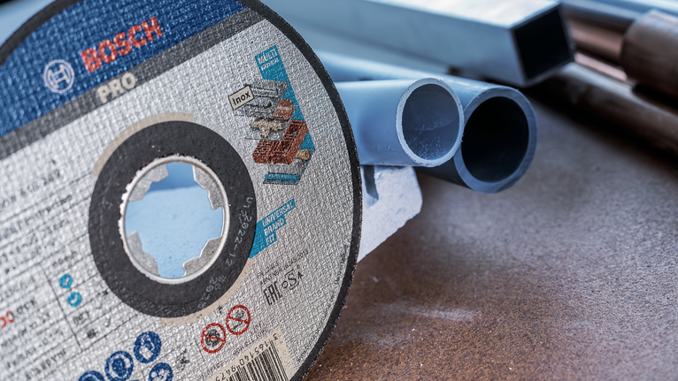 PRO Multi Material X-Lock Cutting Disc, 125 x 1 x 22.23 mm Cutting disc resting on a workbench beside several plastic pipes.