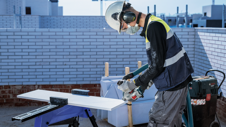 PRO Multi Material X-Lock Cutting Disc, 125 x 1 x 22.23 mm A person wearing safety equipment uses a power tool to cut a board outdoors.