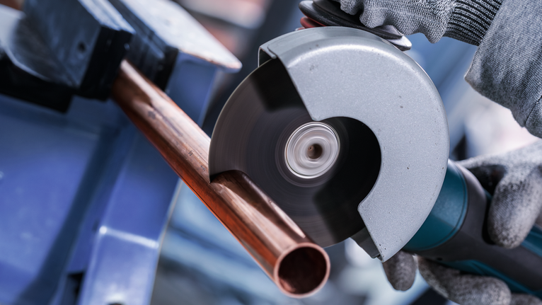 PRO Multi Material X-Lock Cutting Disc, 125 x 1 x 22.23 mm Person wearing safety equipment cuts a copper pipe with an angle grinder.