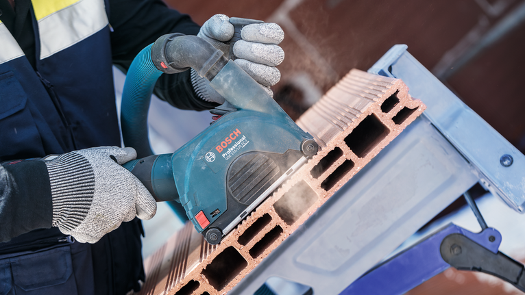 PRO Multi Material X-Lock Cutting Disc, 125 x 1 x 22.23 mm A person wearing safety equipment cuts a hollow brick with a power tool.