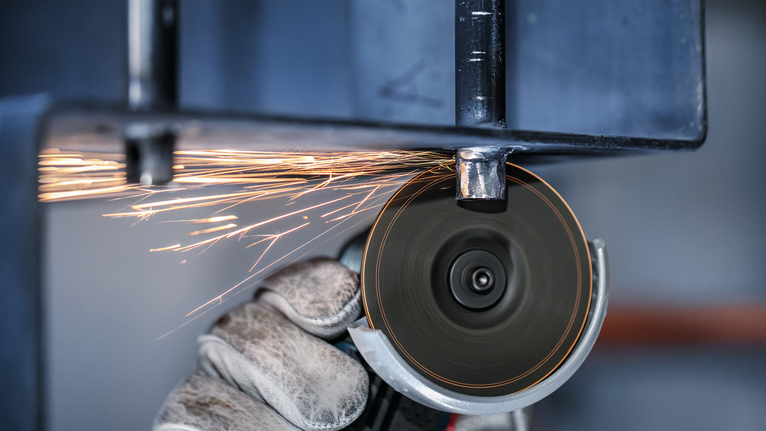 PRO Stainless Steel and Metal Grinding Disc, 76 x 4 x 10 mm Person wearing safety equipment uses an angle grinder to cut metal, producing sparks.