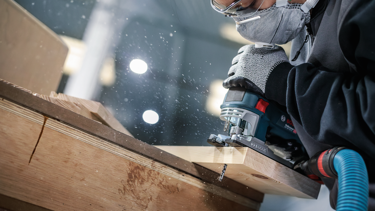 PRO Wood precise T144DP Jigsaw Blade, 100 mm, 5 pcs A person wearing safety equipment uses a jigsaw to cut wood.