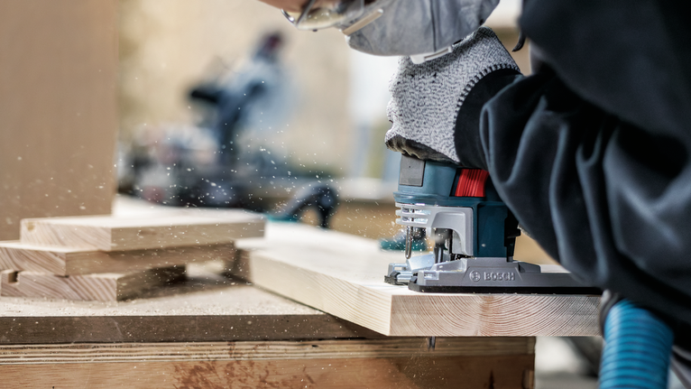 PRO Wood precise T144DP Jigsaw Blade, 100 mm, 5 pcs Person wearing safety equipment uses a jigsaw to cut wooden boards.