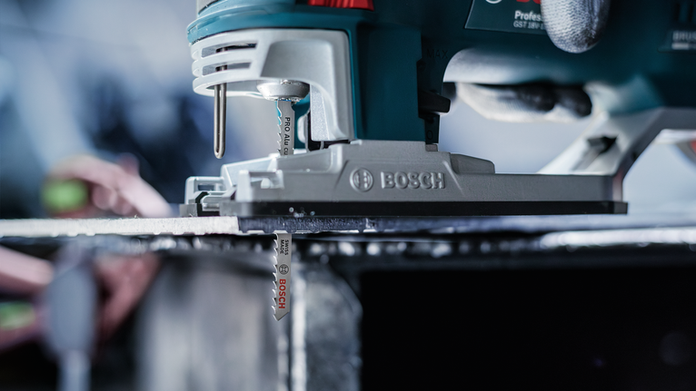 Person wearing safety equipment guides a jigsaw cutting through a metal sheet.