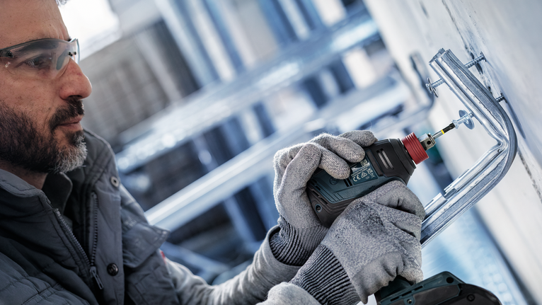 PRO PH Impact Bit, PH1 x 55, PH2 x 55, PH3 x 55 mm, 3 pcs A person wearing safety equipment uses a power drill to fasten a metal bracket to a wall.