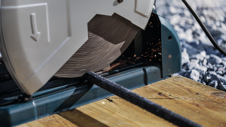 Cut-off saw slicing through a metal rod on a wooden platform.