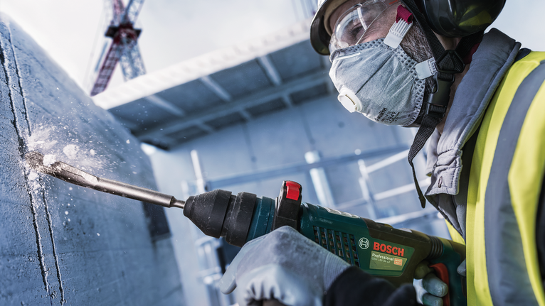 PRO SDS plus Hollow Gouging Chisel, 22 x 250 mm Person wearing safety equipment drills into concrete on a construction site.