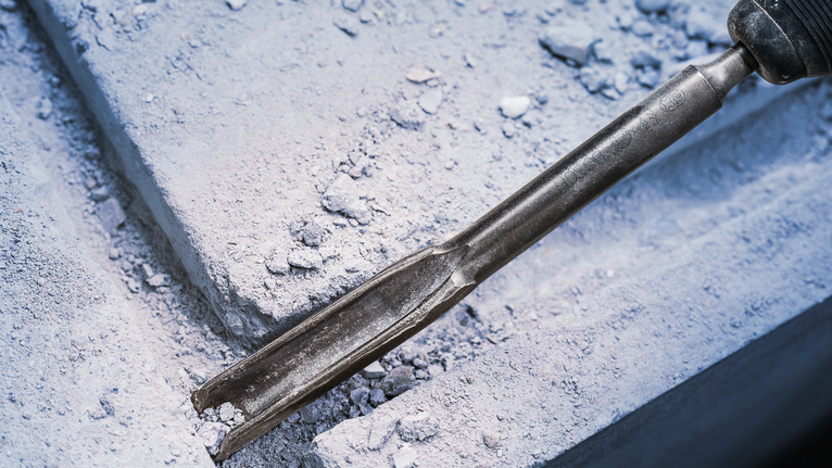 PRO SDS plus Hollow Gouging Chisel, 22 x 250 mm Chisel tool breaking concrete with dust and debris scattered around.