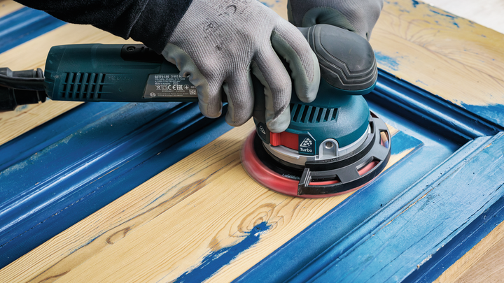 Object #200471072: 7390919_app_web_3 Worker wearing safety equipment sands blue paint from a wooden door.