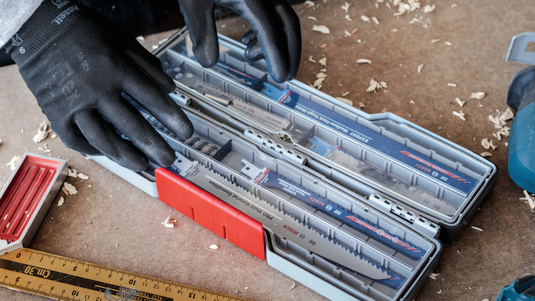 Person wearing safety equipment selects a saw blade from an organized tool case.