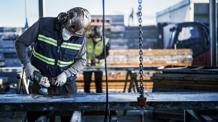 Object #200476264: 3089952_app_web_1 A person wearing safety equipment grinds a metal beam at a construction site.