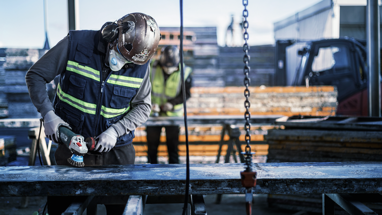 PRO Metal clean Cup Brush, 75 x 0.3 mm, Thread A person wearing safety equipment grinds a metal beam at a construction site.