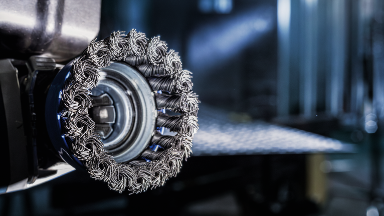 Close-up of a wire brush wheel attachment on a power tool in a workshop.
