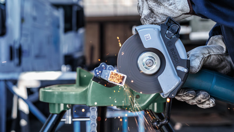 Person wearing safety equipment cuts metal pipe with an angle grinder, sparks flying.