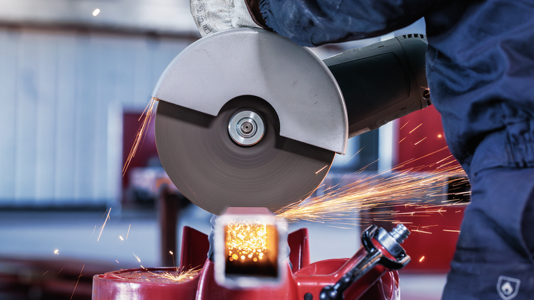 Person wearing safety equipment uses an angle grinder to cut metal, creating sparks.