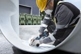 A person wearing safety equipment grinds the interior of a large metal pipe.
