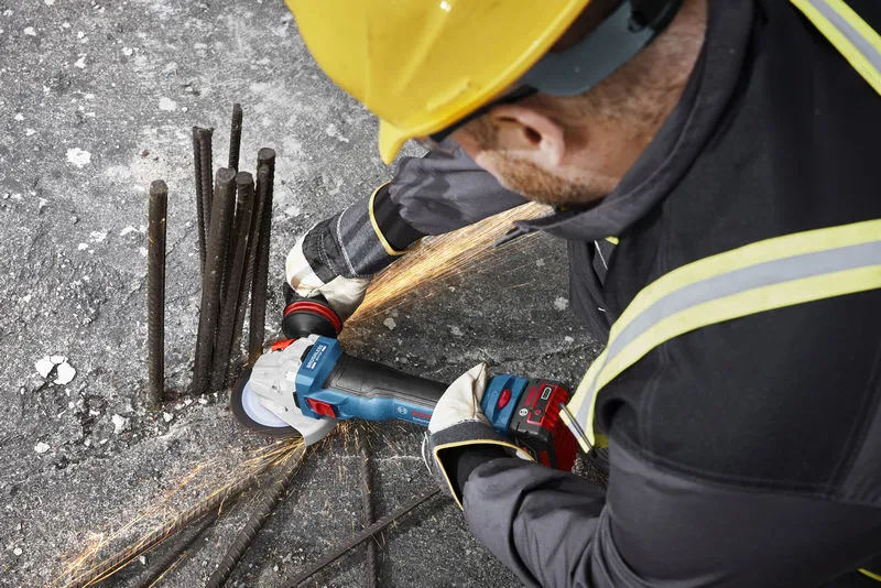 GWS 18V-11 S A person wearing safety equipment grinds rebar on concrete with a cordless angle grinder.