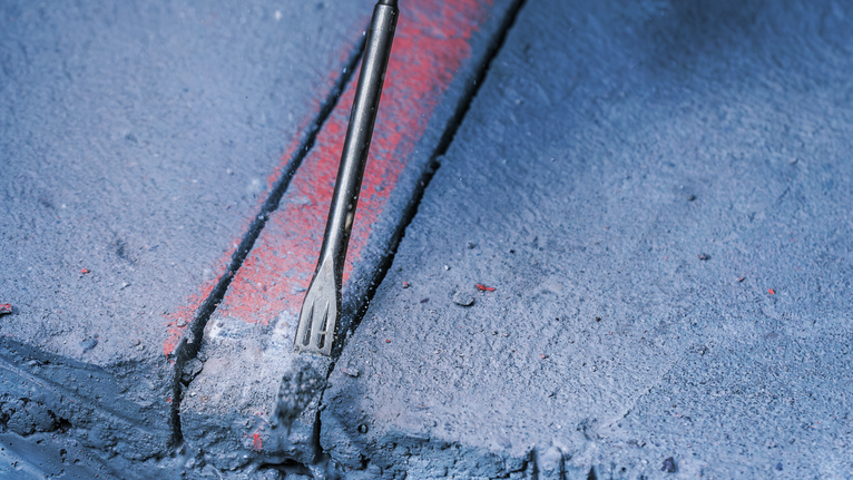 Chisel bit breaking a groove into a concrete surface.