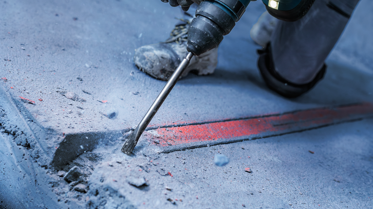 A person wearing safety equipment uses a rotary hammer to break concrete.