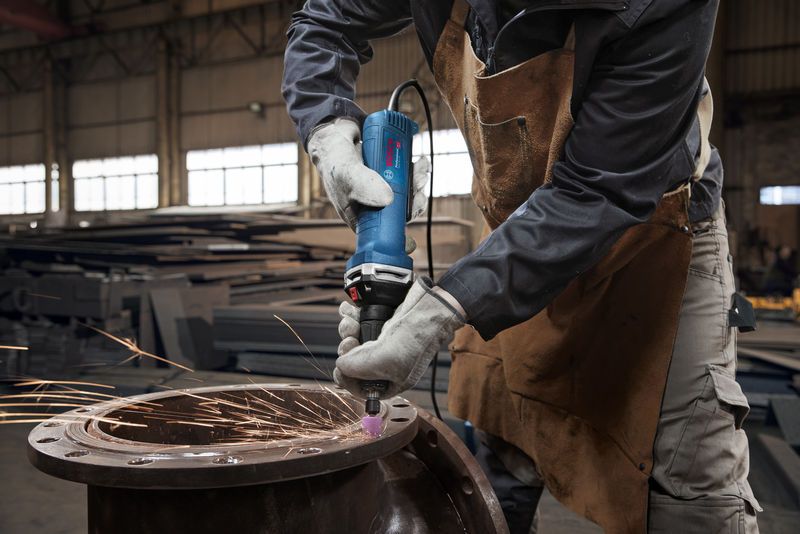 A person wearing safety equipment grinds metal with a straight grinder, producing sparks.