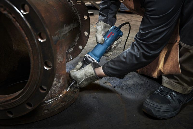 A person wearing safety equipment uses a straight grinder on a metal flange.