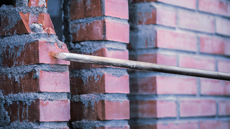 PRO SDS max-4C Pointed Chisel Set, 400 mm, 10 pcs Chisel breaking through a red brick wall for demolition work.