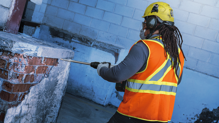 PRO SDS max-4C Pointed Chisel Set, 400 mm, 10 pcs Person wearing safety equipment uses a demolition tool to break concrete and brick.