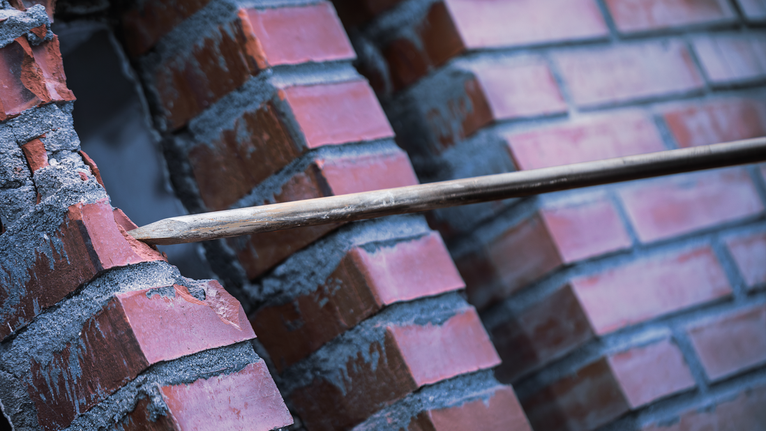 PRO SDS max-4C Pointed Chisel Set, 400 mm, 10 pcs Pointed chisel breaking through a red brick wall.