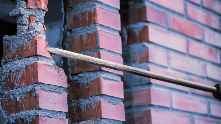 PRO SDS max-4C Pointed Chisel Set, 400 mm, 10 pcs Chisel tool breaking through a red brick wall.