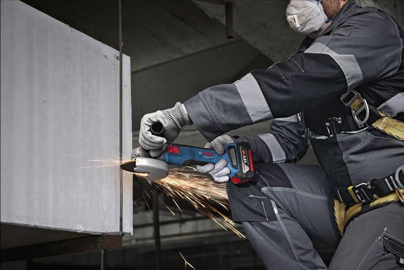 A person wearing safety equipment grinds a concrete edge with an angle grinder.