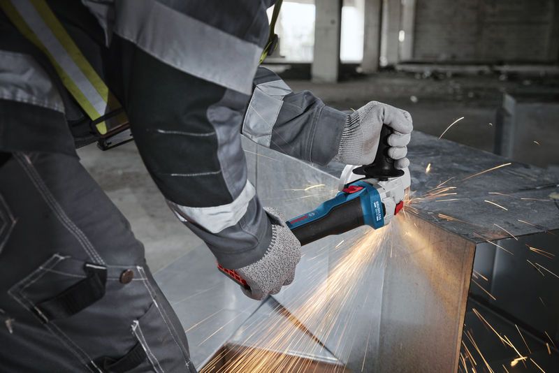 GWS 18V-8 A person wearing safety equipment grinds a metal slab, producing bright sparks.
