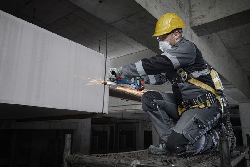 GWS 18V-8 A person wearing safety equipment grinds concrete with a power tool on a construction site.