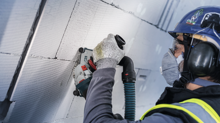 PRO Ceramic Diamond Disc, 105 x 20/16 mm Person wearing safety equipment grinds into a concrete wall using a power tool.
