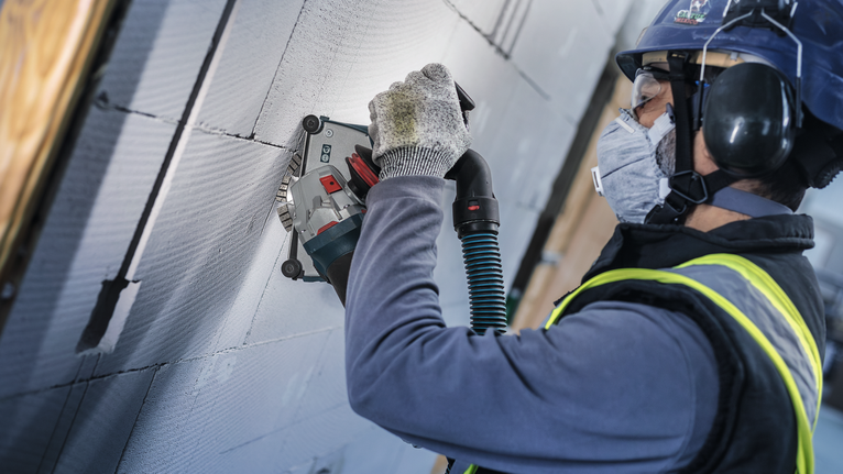 PRO Ceramic Diamond Disc, 105 x 20/16 mm Person wearing safety equipment uses a wall chaser to cut grooves in a concrete wall.