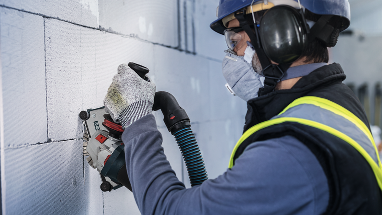 PRO Ceramic Diamond Disc, 105 x 20/16 mm Person wearing safety equipment grinds a wall with a power tool.