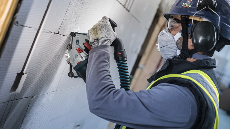 PRO Ceramic Diamond Disc, 105 x 20/16 mm Person wearing safety equipment uses a wall chaser to cut grooves in concrete blocks.