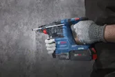 A person wearing safety equipment drills into a concrete wall using a rotary hammer.