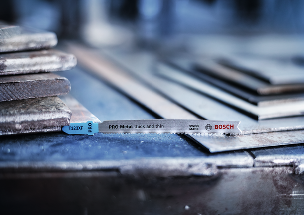 PRO Metal thick and thin T123XF Jigsaw Blade, 100 mm, 3 pcs Jigsaw blade placed on stacked metal sheets in a workshop.