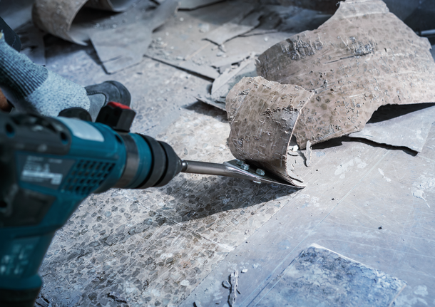 Person wearing safety equipment removes floor tiles with a power chisel.