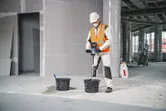 A person wearing safety equipment uses a stirring mechanism to mix material in a bucket.