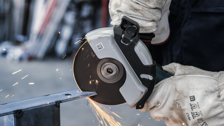 PRO Stainless Steel and Metal Bonded Cutting Disc, 125 x 1.6 x 22.23 mm, X-Lock, Straight, oSa Person wearing safety equipment cuts metal with an angle grinder, producing sparks.