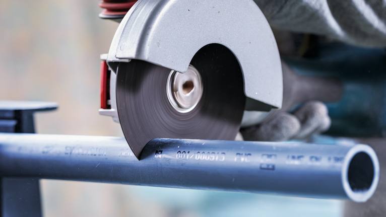 PRO Multi Material X-Lock Cutting Disc, 125 x 1 x 22.23 mm Circular saw cutting a blue plastic pipe, worker wearing safety equipment.