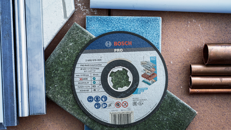 PRO Multi Material X-Lock Cutting Disc, 125 x 1 x 22.23 mm Cutting disc placed on colored tiles, surrounded by metal and plastic pipes.
