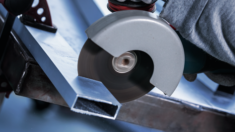 PRO Multi Material X-Lock Cutting Disc, 125 x 1 x 22.23 mm Person wearing safety equipment cuts a metal beam with an angle grinder.