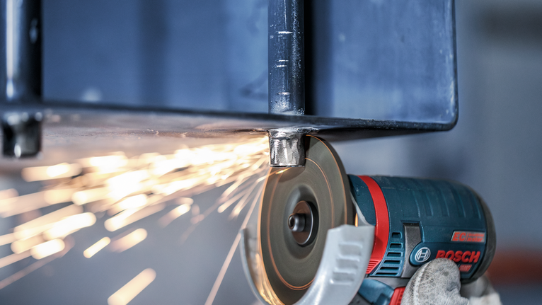 PRO Stainless Steel and Metal Grinding Disc, 76 x 4 x 10 mm Gloved worker wearing safety equipment grinds a metal beam with an angle grinder, producing sparks.